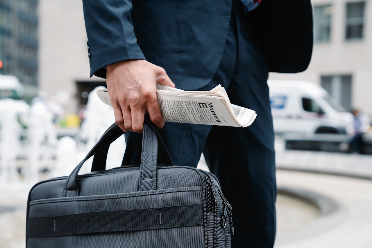 Close-up Photo of Person carrying Black Hand Bag and Newspaper