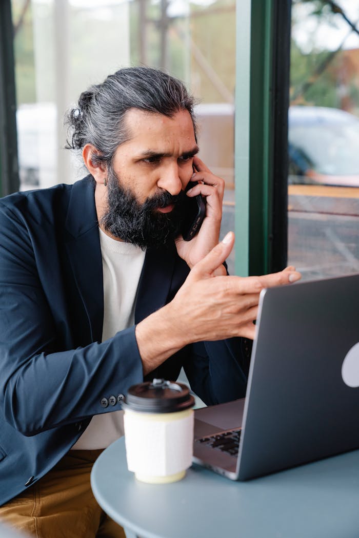 Man talking on Phone while looking at a Laptop 